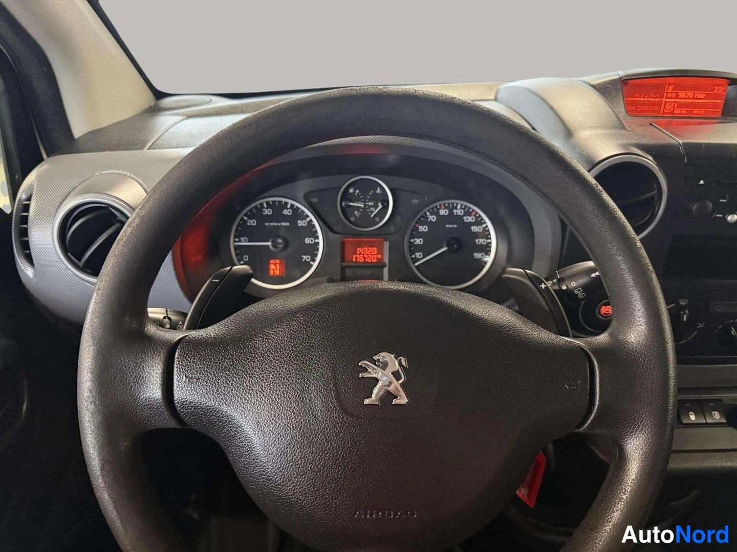 Muu: Ohjauspyörä Peugeot-leijonamerkillä, sen takana mittaristo, jonka oranssi näyttö lukee 14328 ja 176720 km; kuvassa näkyvät myös ilmastointituuletusaukko ja radi