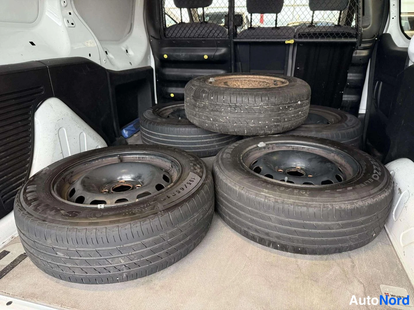 Yksityiskohta: Pakolaautojen tavaratilassa on useita irrotettuja renkaita; yhden renkaan sivussa lukee '195/65 R15'.