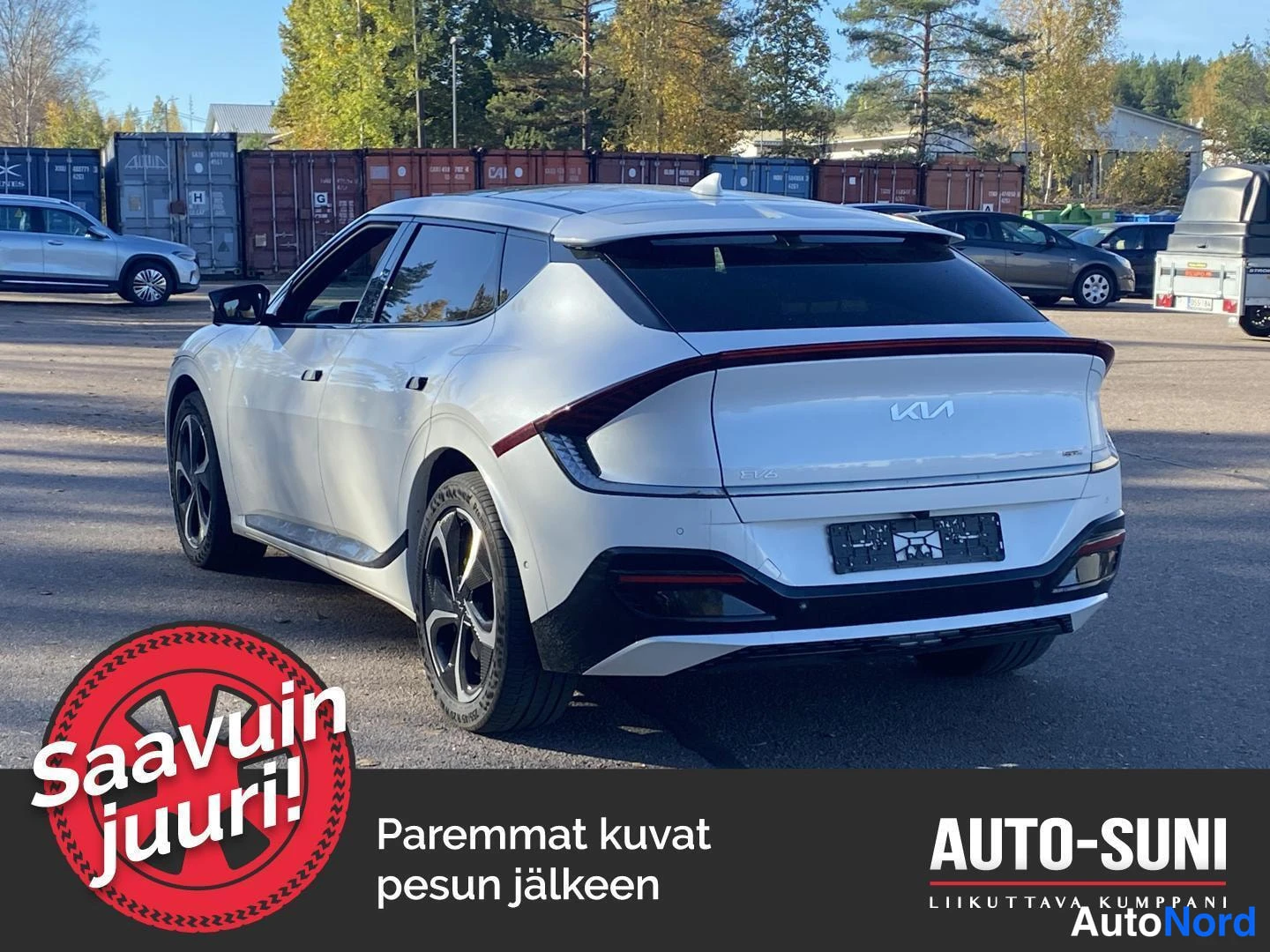Takaviisto: Valkoinen henkilöauto kuvattuna takaosan ja kyljen kulmasta: peräovessa KIA-merkki ja poikittainen takavalo, kattospoileri sekä tummat kevytmetallivanteet.