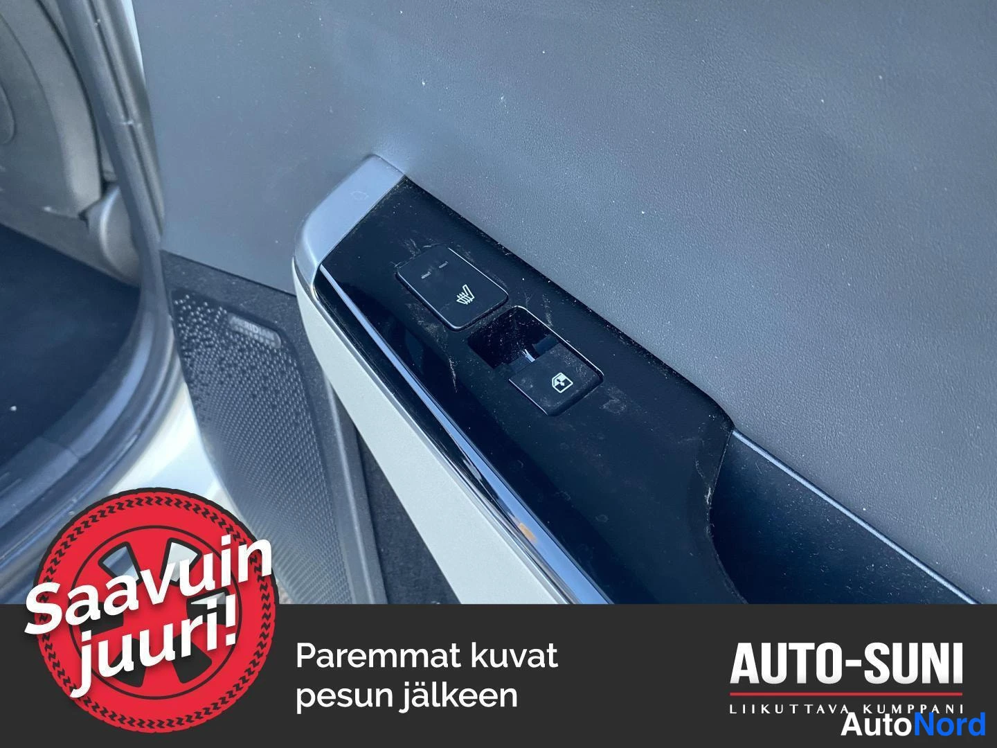 Muu: Sisäkuva auton oven kahvan alueesta: oven lukituksen ja istuimenlämmityksen painikkeet, vasemmalla näkyy kaiuttimen verkko ja valkoista koria.