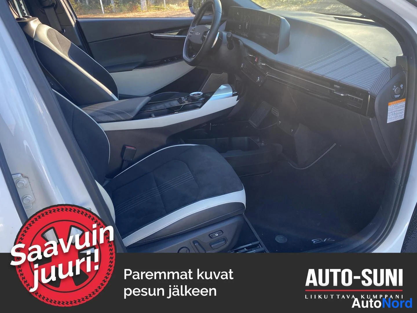 Muu: Auton sisätila kuljettajan oven puolelta: tummat etupenkit, Kia-ohjauspyörä ja kojelaudan kaareva näyttö.
