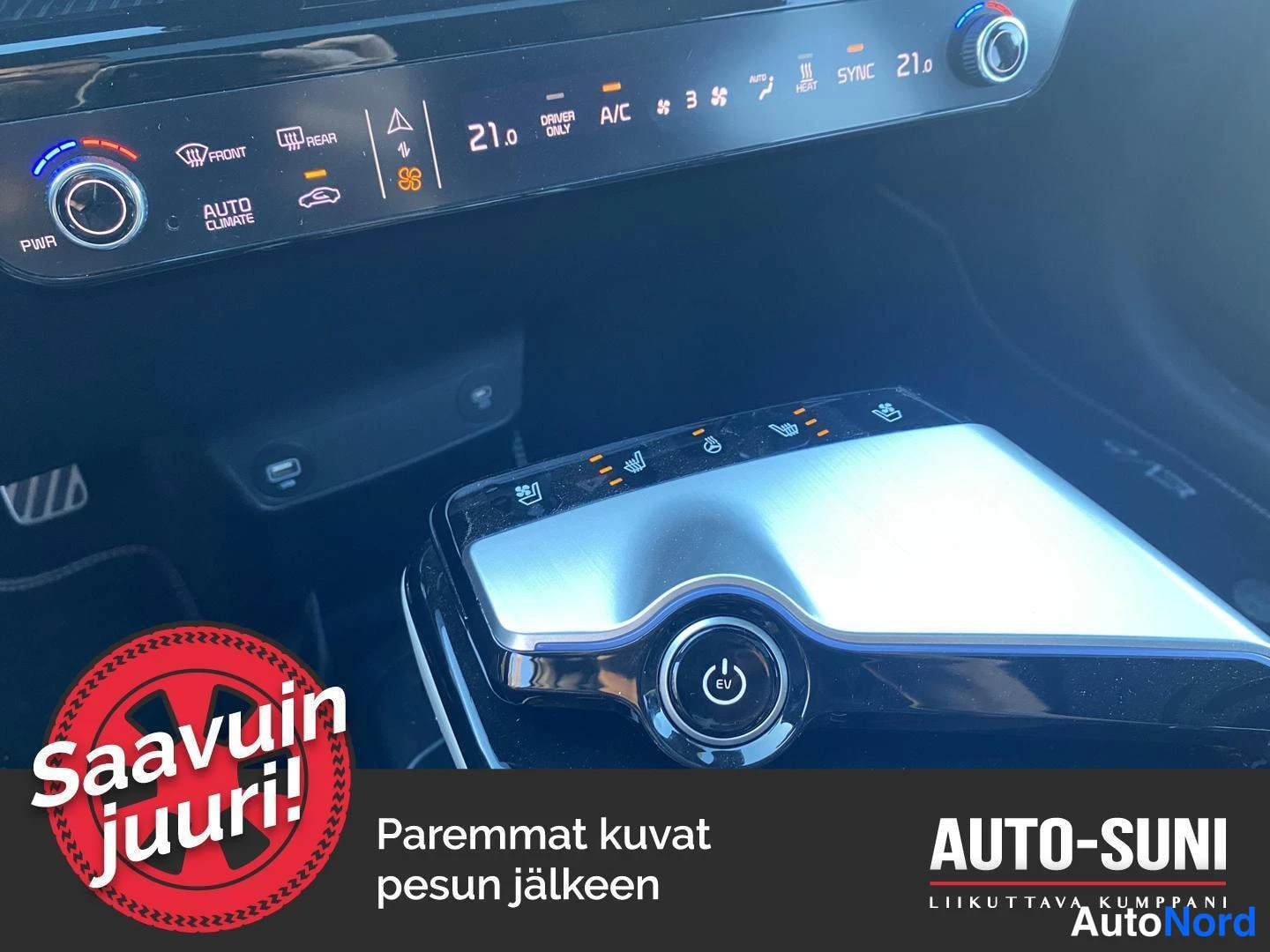 Yksityiskohta: Kia EV6:n sisätilat: ilmastoinnin kosketuspaneeli, jossa tekstit AUTO CLIMATE, A/C ja SYNC sekä arvo 21,0, ja keskikonsoli, jossa istuinlämmitys- ja tuuletusnäp