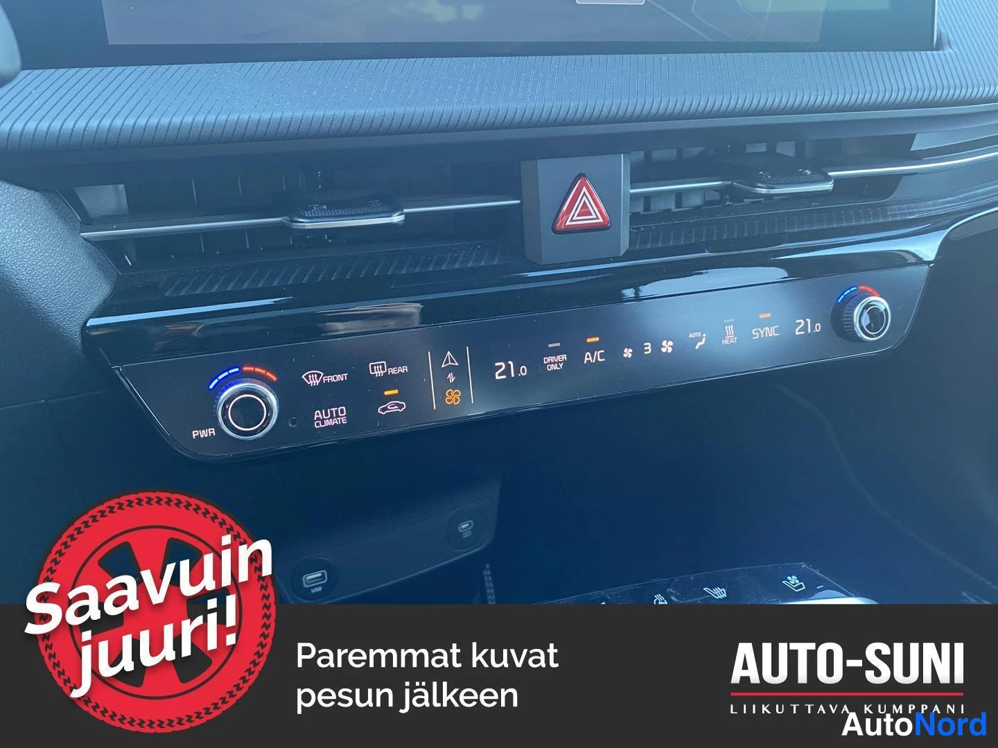 Yksityiskohta: Kia EV6:n kojetaulu lähikuvassa: ilmastoinnin kosketuspaneeli (AUTO CLIMATE, 21,0, A/C, SYNC), varoitusvalon kolmionappi, ilmastointisuuttimet ja USB-portti kes