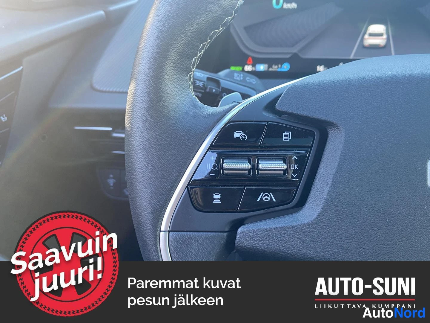 Yksityiskohta: Kia EV6:n ohjauspyörän oikean puolen näppäimet lähikuvassa: ajoavustus- ja tietonäppäimet, OK-säädin ja kaistapysyvyysavustimen kuvake; taustalla kojetaulun näy