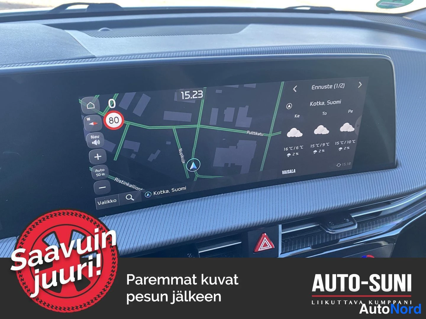 Muu: Kojelaudan infotainment-näyttö, jossa näkyy navigointikartta Kotkan alueelta ja kolmen päivän sääennuste; kuvan alaosaan on lisätty myyjän mainosmerkintä.