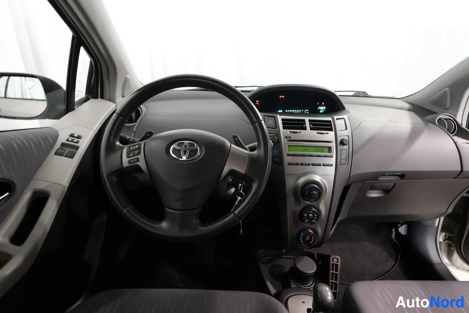 Muu: Ohjaamo Toyota Yarisista: ohjauspyörä ja kojelaudan keskusyksikkö, vaihteenvalitsin keskustassa.