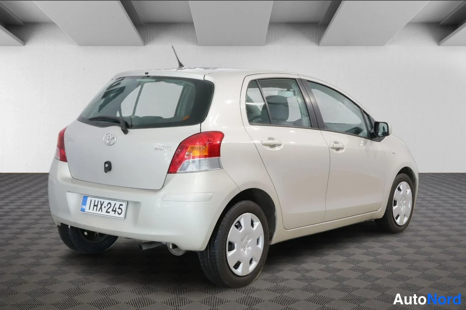 Takaviisto: Vaaleanbeige Toyota Yaris -henkilöauto kuvattuna viistosti takaa, rekisterikilpi.