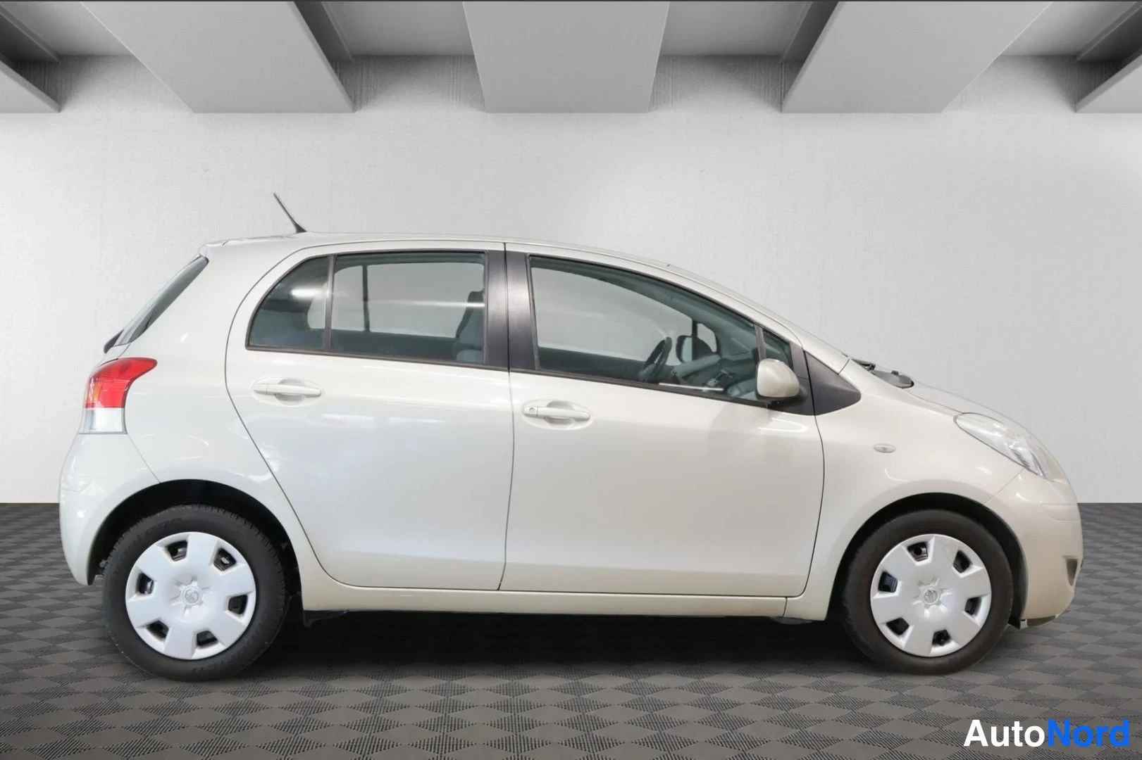 Sivulta: Vaaleanbeige Toyota Yaris -henkilöauto sivuprofiilikuvassa.