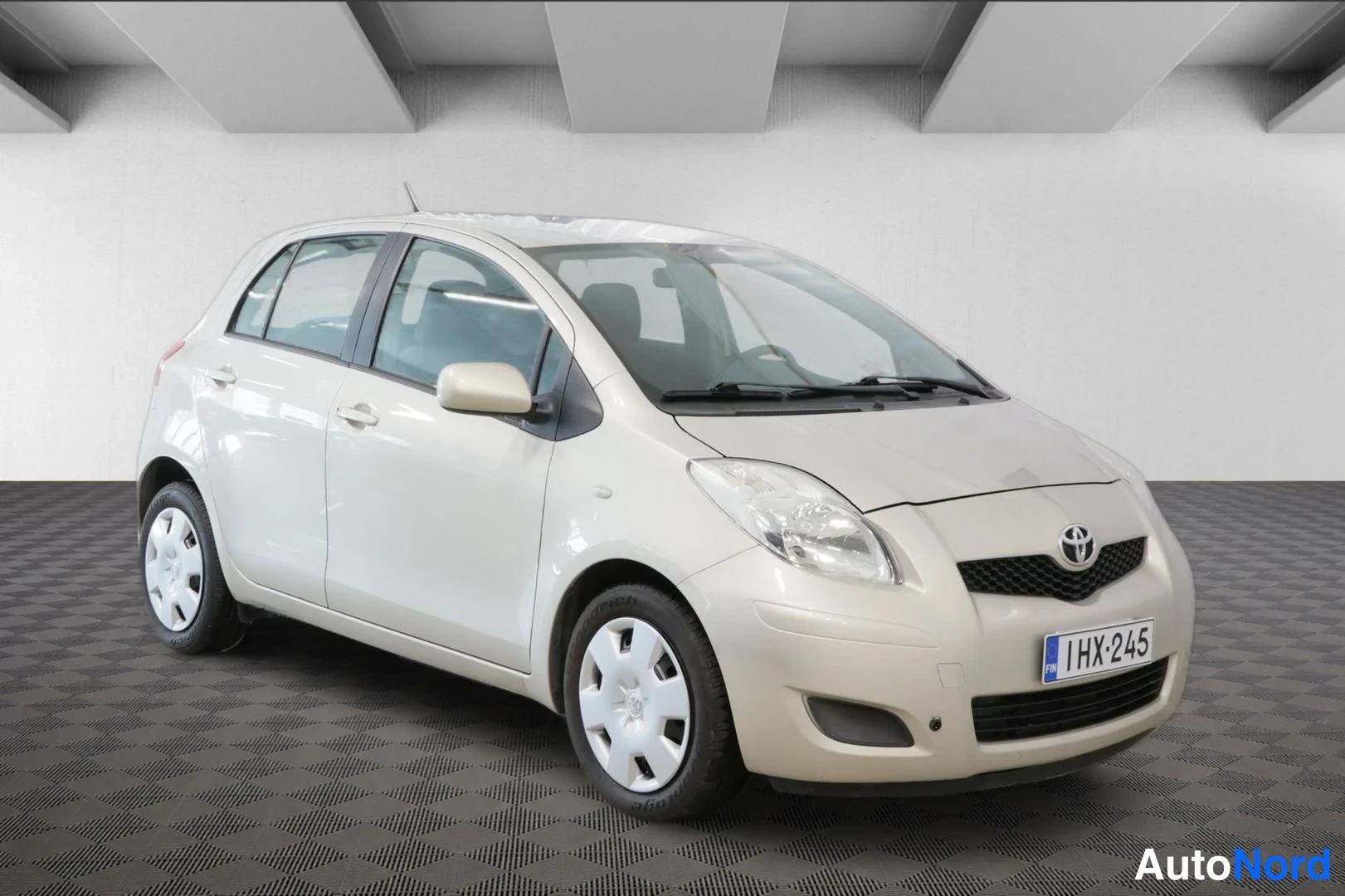 Etuviisto, nokka oikealle: Vaaleanbeige Toyota Yaris -henkilöauto kuvattuna viistosti edestä oikealta, rekisterikilpi.