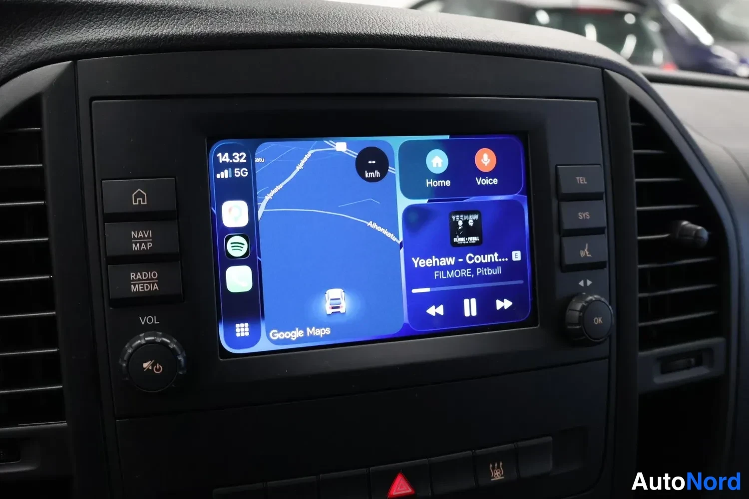 Muu: Auton kojelaudan infotainment-näyttö, jossa näkyy Google Maps -navigaatio, Spotify ja musiikkisoitin, etupaneelin painikkeet NAVI MAP ja RADIO MEDIA ympärillä.