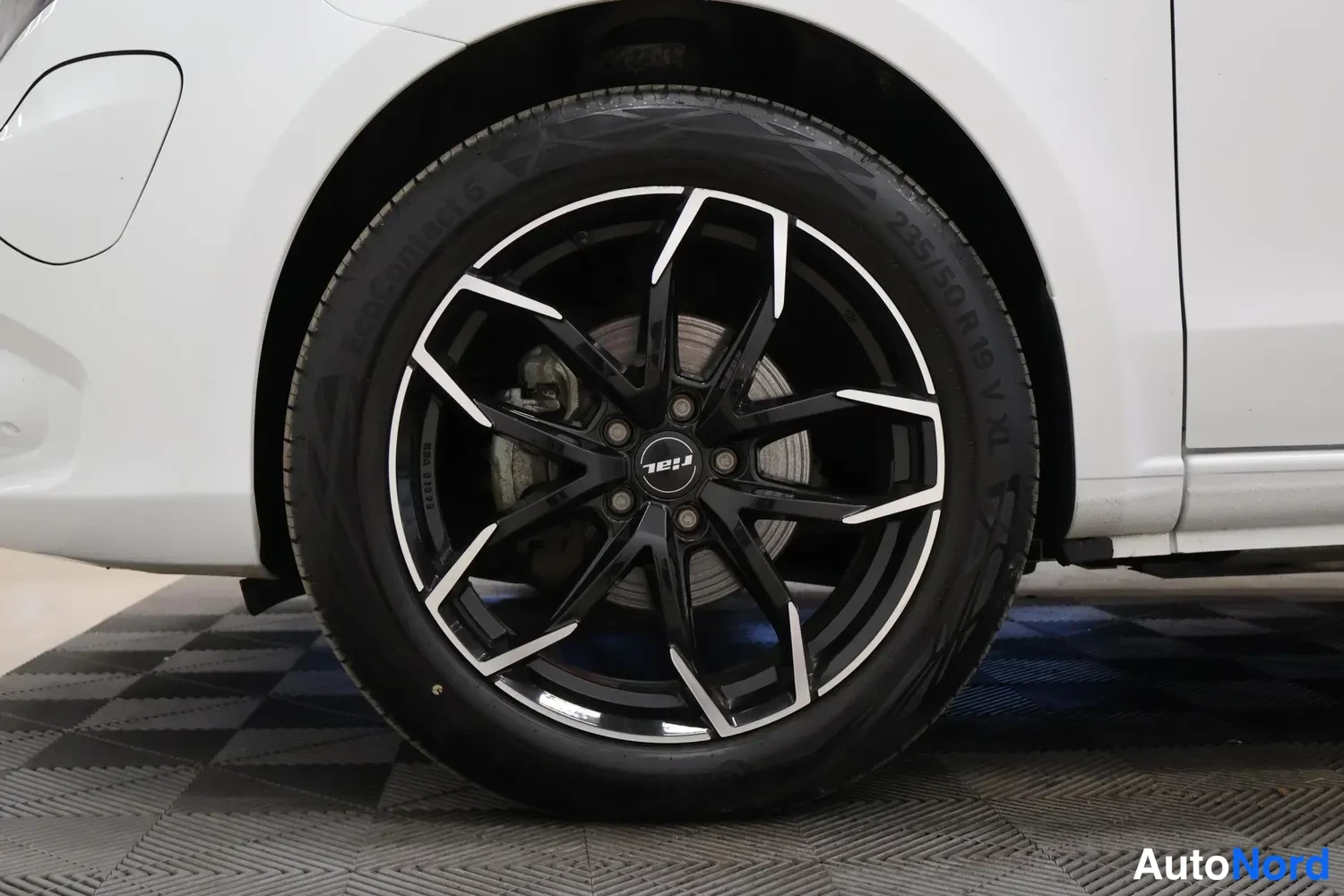 Sivulta: Sivukuva valkoisen auton etupyörästä, musta kiiltävä pöydätähti-vanne, Continental EcoContact 6 -rengas, kokomerkintä 235/50 R19 V XL luettavissa renkaan sivuss