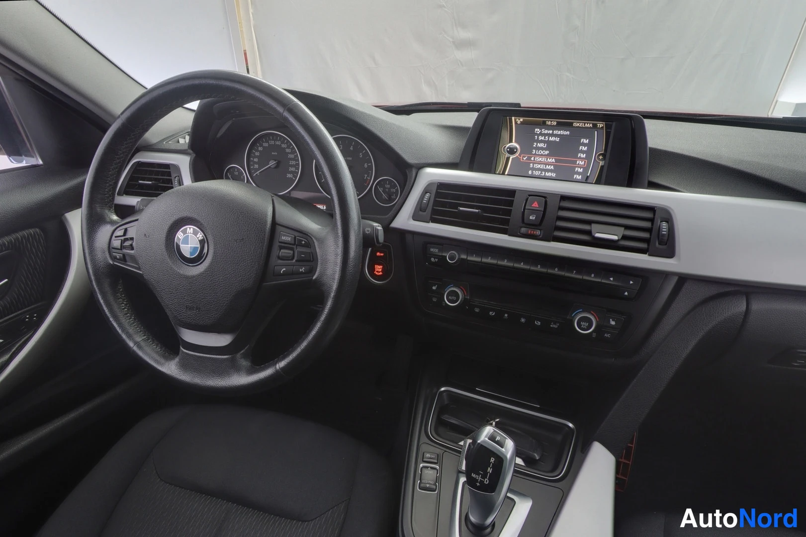 Muu: BMW:nn auton ohjaamo: ohjauspyörä, mittaristo, keskikonsoli ja radiossa näkyvä radiolistavalikko.