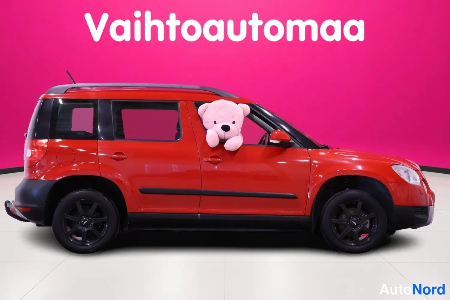 Etuviisto, nokka oikealle: Punainen Skoda Yeti sivukulmasta keula oikealla; kattokaiteet ja mustat vanteet, nalleikkuna törröttää ikkunasta.