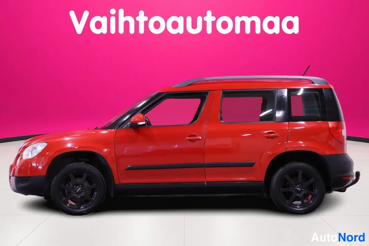 Etuviisto, nokka vasemmalle: Punainen tila-auton kylki ja etuosa kuvattuna kolmannelta, mustat vanteet, tummat kattokaiteet ja kattospoilerit.