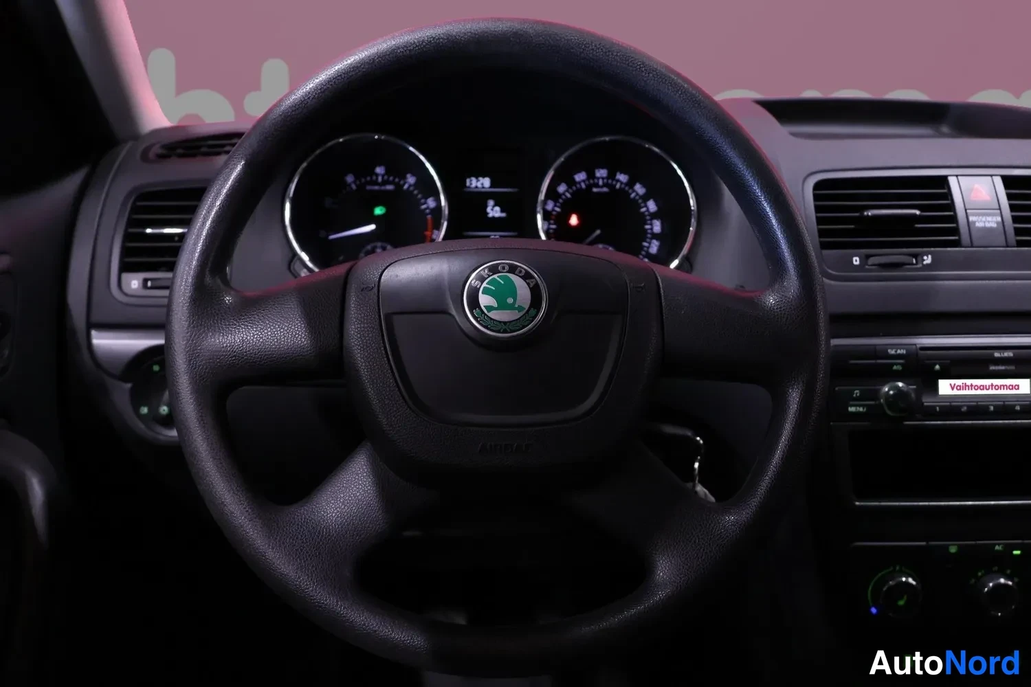 Muu: Ohjauspyörä ja kojelauta: Skoda-merkillä varustettu ohjauspyörä, takanamittarit, radio ja ilmastointisäätimet näkyvissä.