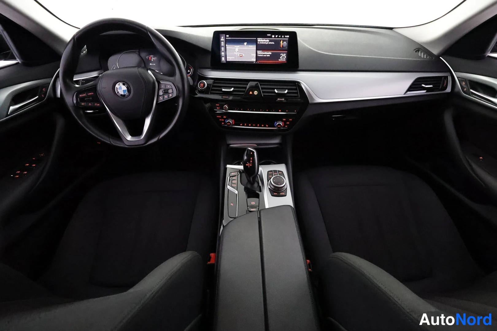 Sivulta: Kojetaulu suoraan edestä: BMW-merkkinen ohjauspyörä, keskellä karttanaavigaatiota näyttävä infotainment-näyttö, automaattivaihteen valitsin ja kierto-ohjain kes