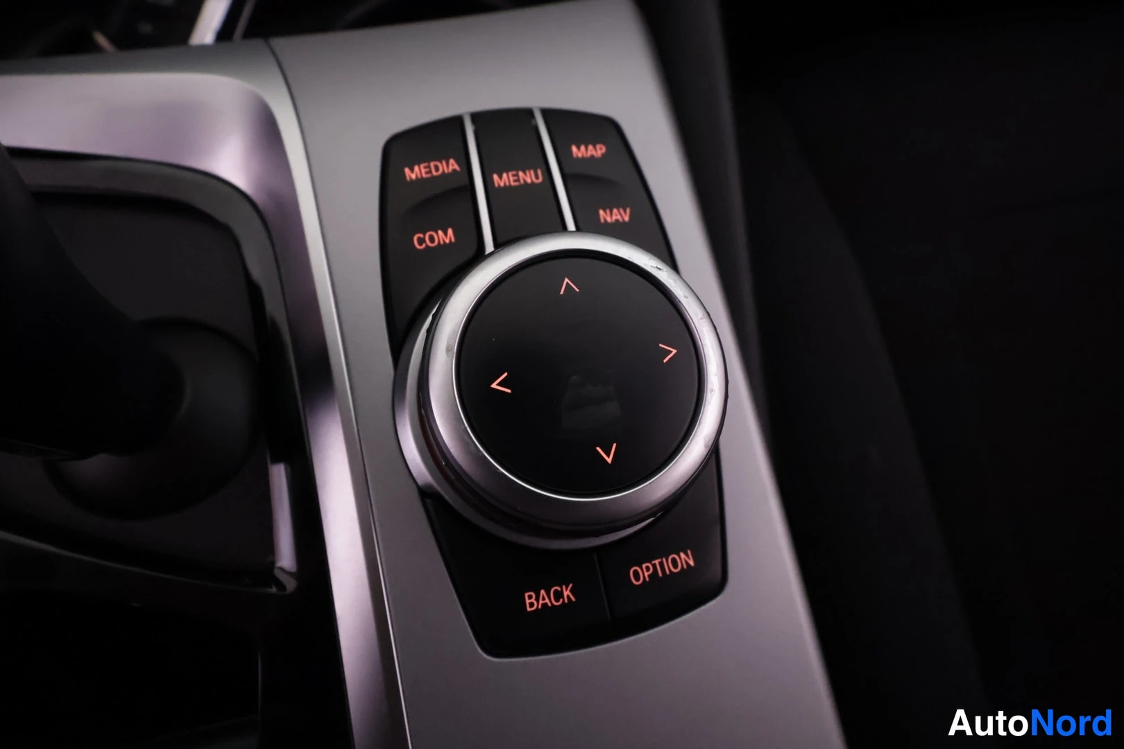 Sivulta: Sisätiloissa: BMW:n iDrive-ohjausnuppi ja ympäröivät MEDIA-, MENU-, MAP-, COM-, NAV-, BACK- ja OPTION-painikkeet.