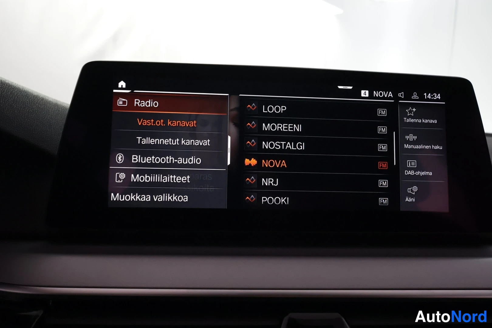 Yksityiskohta: Ajonäytön infotainment-näyttö, jolla näkyy radiovalikko tallennettuine kanavineen (LOOP, MOREENI, NOSTALGI, NOVA, NRJ, POOKI) sekä Bluetooth-audio- ja Mobiilila