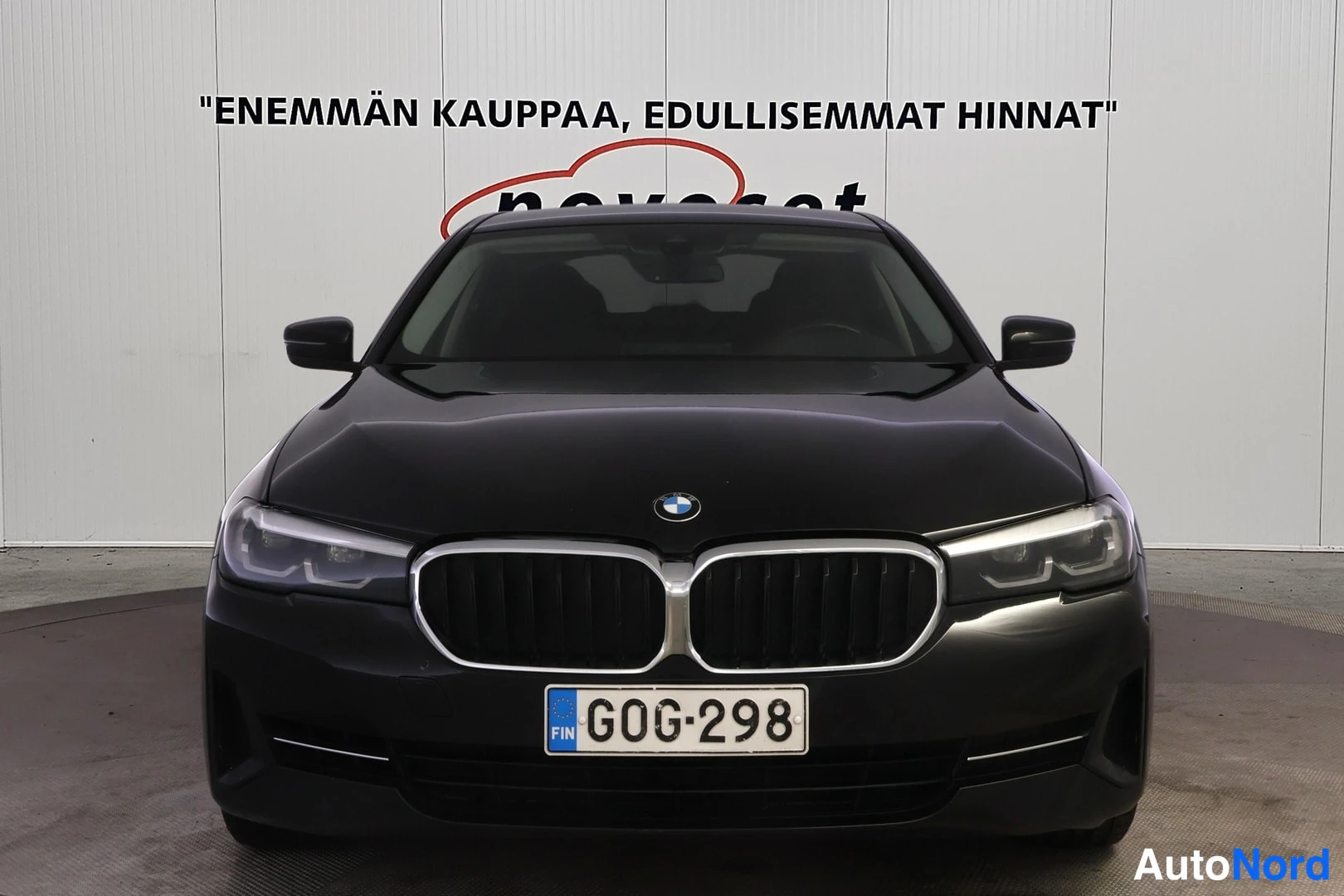 Edestä: Mustan sedanin suora etunäkymä: BMW-merkki, leveä etusäleikkö, ajovalot ja rekisterikilpi.