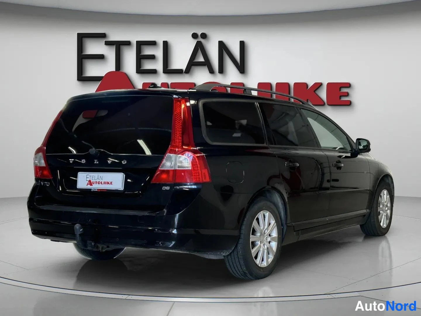 Takaviisto: Musta Volvo V70 -farmari takakulmasta kuvattuna: näkyvät punaiset takavalojen, VOLVO-kirjaimin ja V70- ja D5-merkein varustettu takaluukku, vetokoukun ängä taka