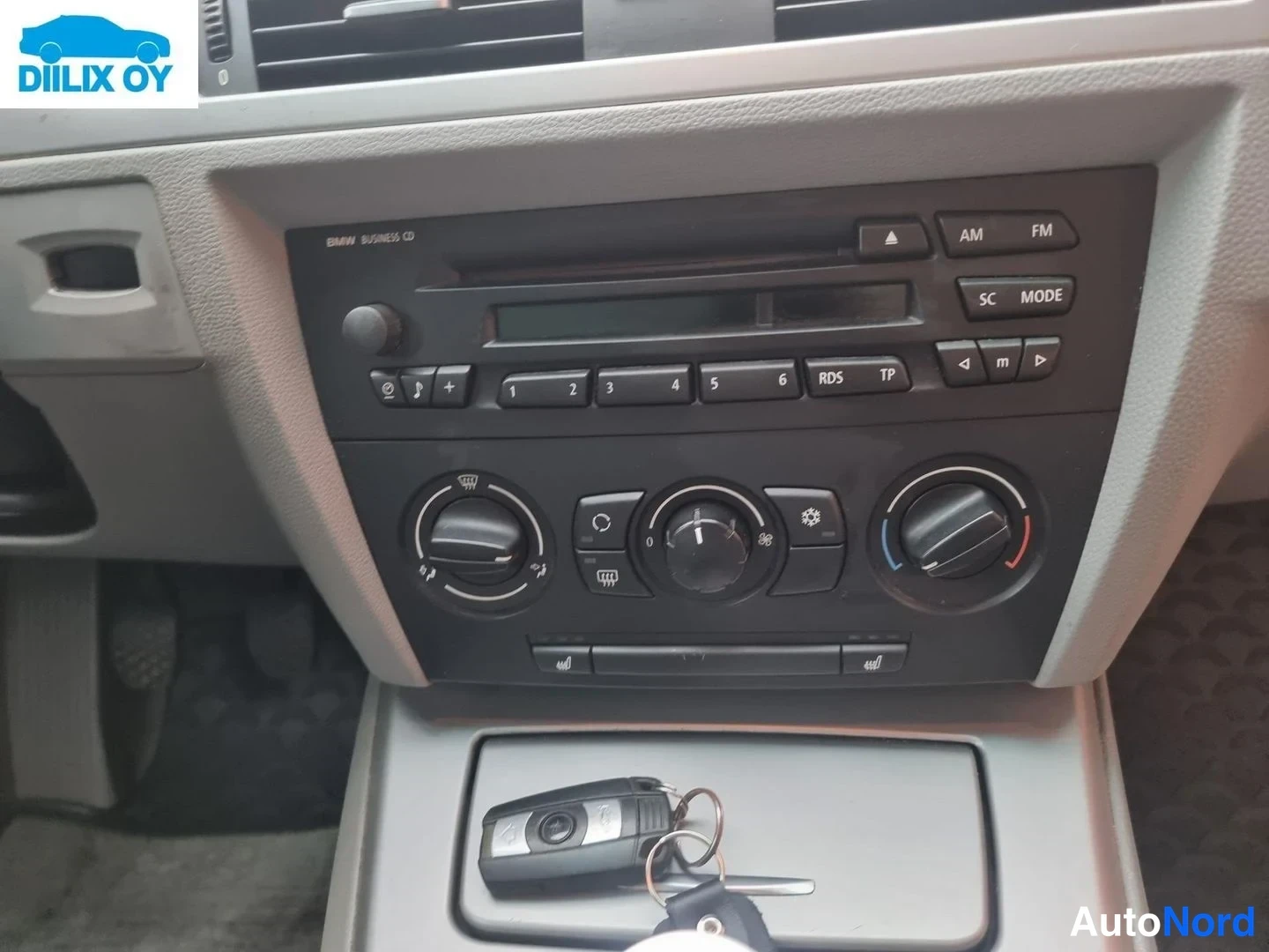 Yksityiskohta: Auton kojelaudan keskiosa ja radio: BMW Business CD -yksikkö painikkeineen ja ilmastointisäätimineen, avain ripustettuna etupaneeliin.