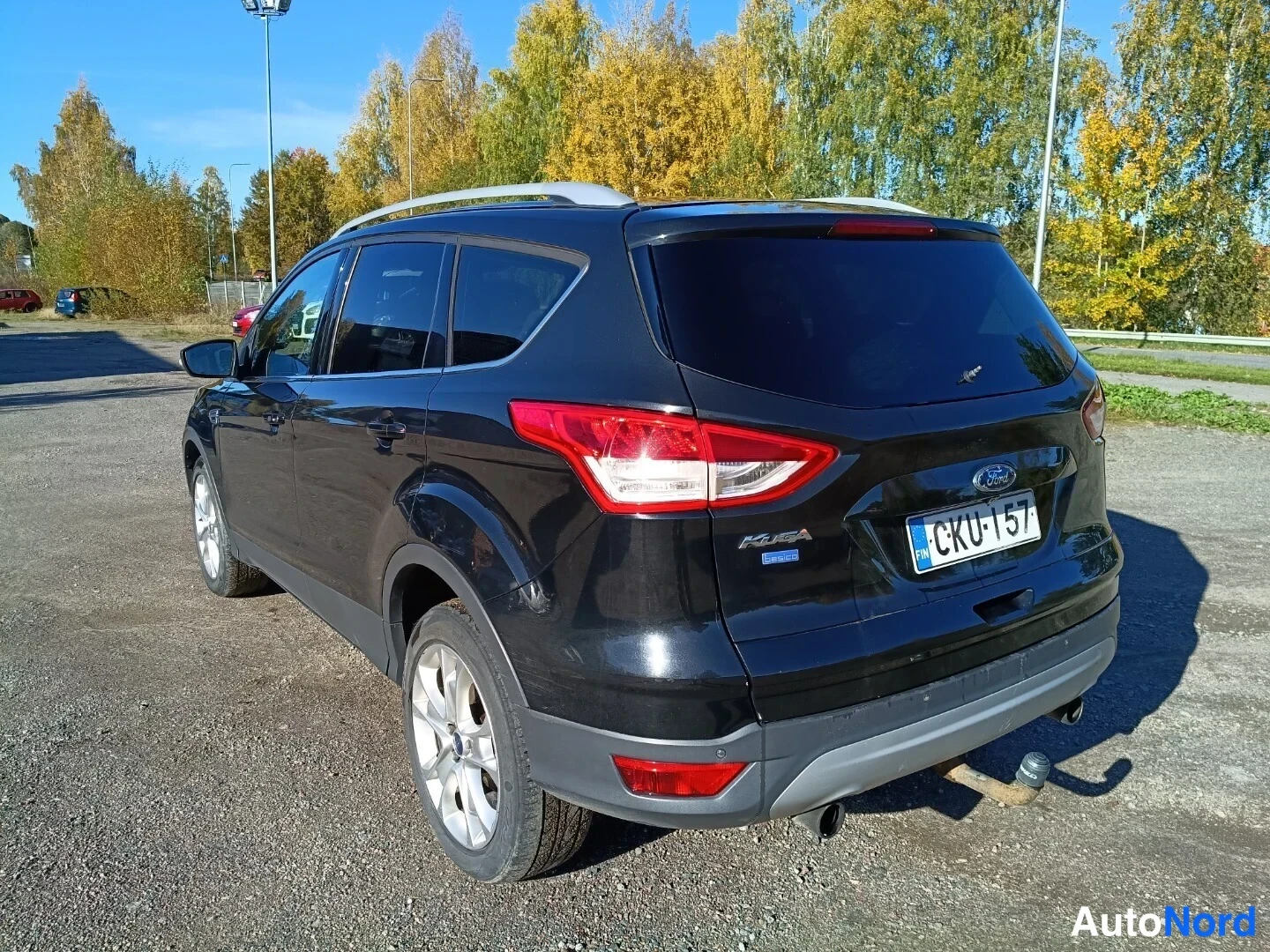 Takaviisto: Musta Ford Kuga kuvattuna takavasemmalta kolmasosakulmasta: takavalot, takaluukku ja Ford-merkki näkyvät, katolla hopeiset kattokaiteet ja rekisteritunnus luett