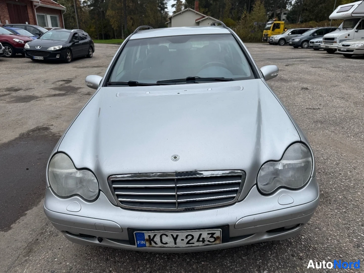 Edestä: Mercedes-Benz-farmarin suora etunäkymä; hopeassa kiiltävä etusäleikkö, pyöreät ajovalot ja EU-rekisterikilpi.