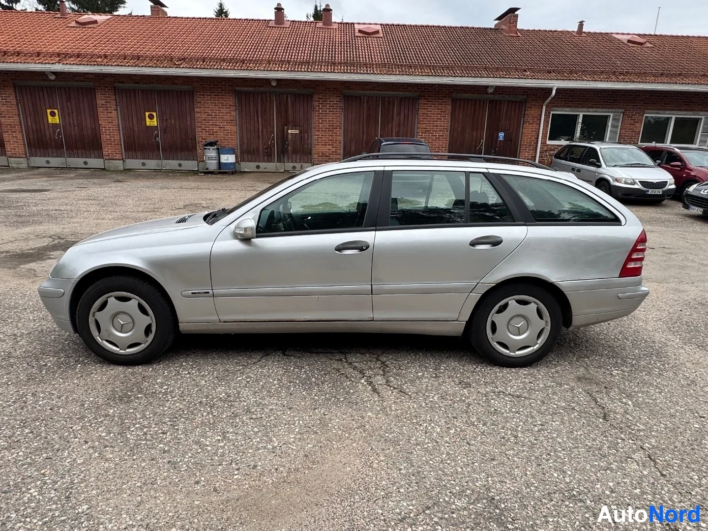 Takaviisto: Valkohopea farmariliina-auto parkkipaikalla, auton kylki ja takaosa näkyvät.