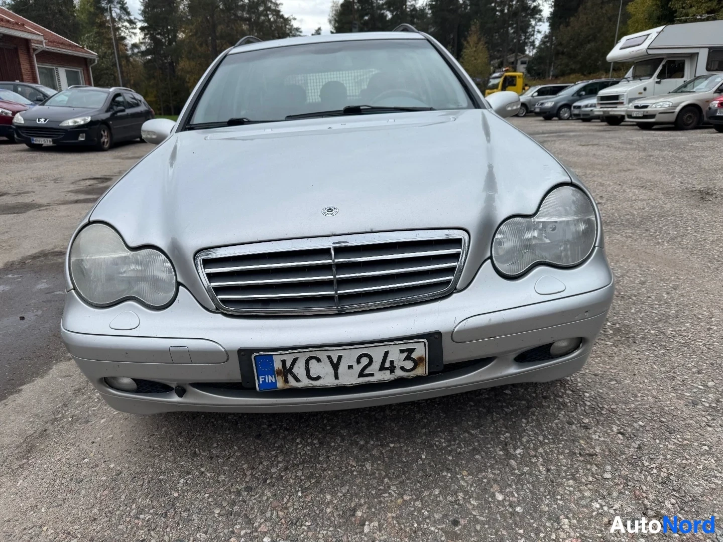 Edestä: Mercedes-Benz-farmarin etunäkymä lähikuvassa; kromikehyksinen etusäleikkö, ajovalot, sumuvalot ja FIN-tunnuksellinen rekisterikilpi.