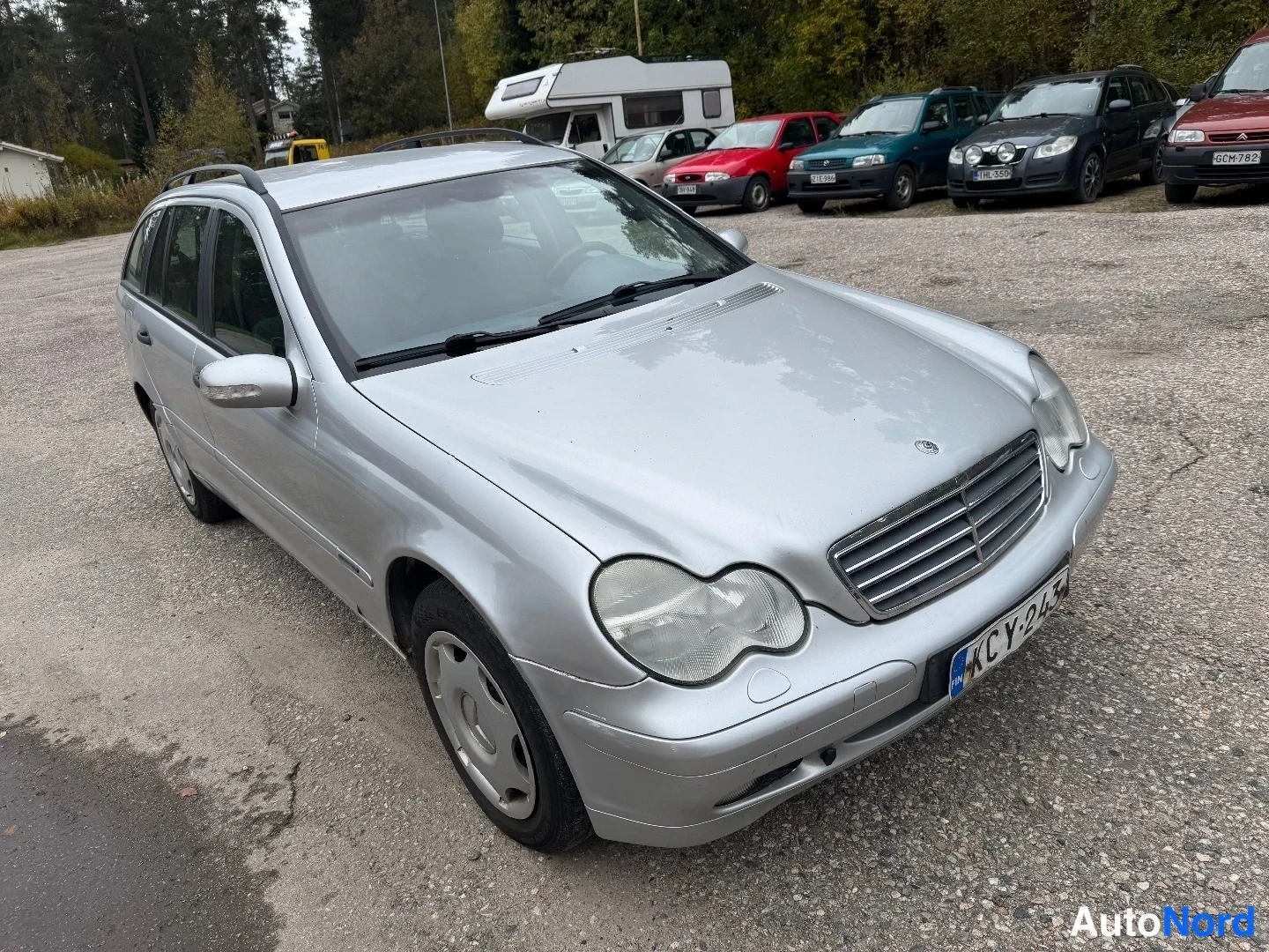 Etuviisto, nokka oikealle: Hopeanvärinen Mercedes-Benz-farmari kuvattuna vinosti edestä, keula kuvan oikealla laidalla; näkyvät etusäleikkö, ajovalot, sivupeilit, rekisterikilpi ja