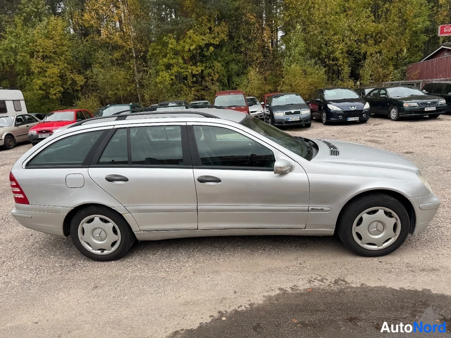 Takaviisto: Hopeanvärinen Mercedes-Benz farmarivaihtoehto sivulta selkä vasemmalla, kattokaiteet ja takavalon reuna näkyvät.
