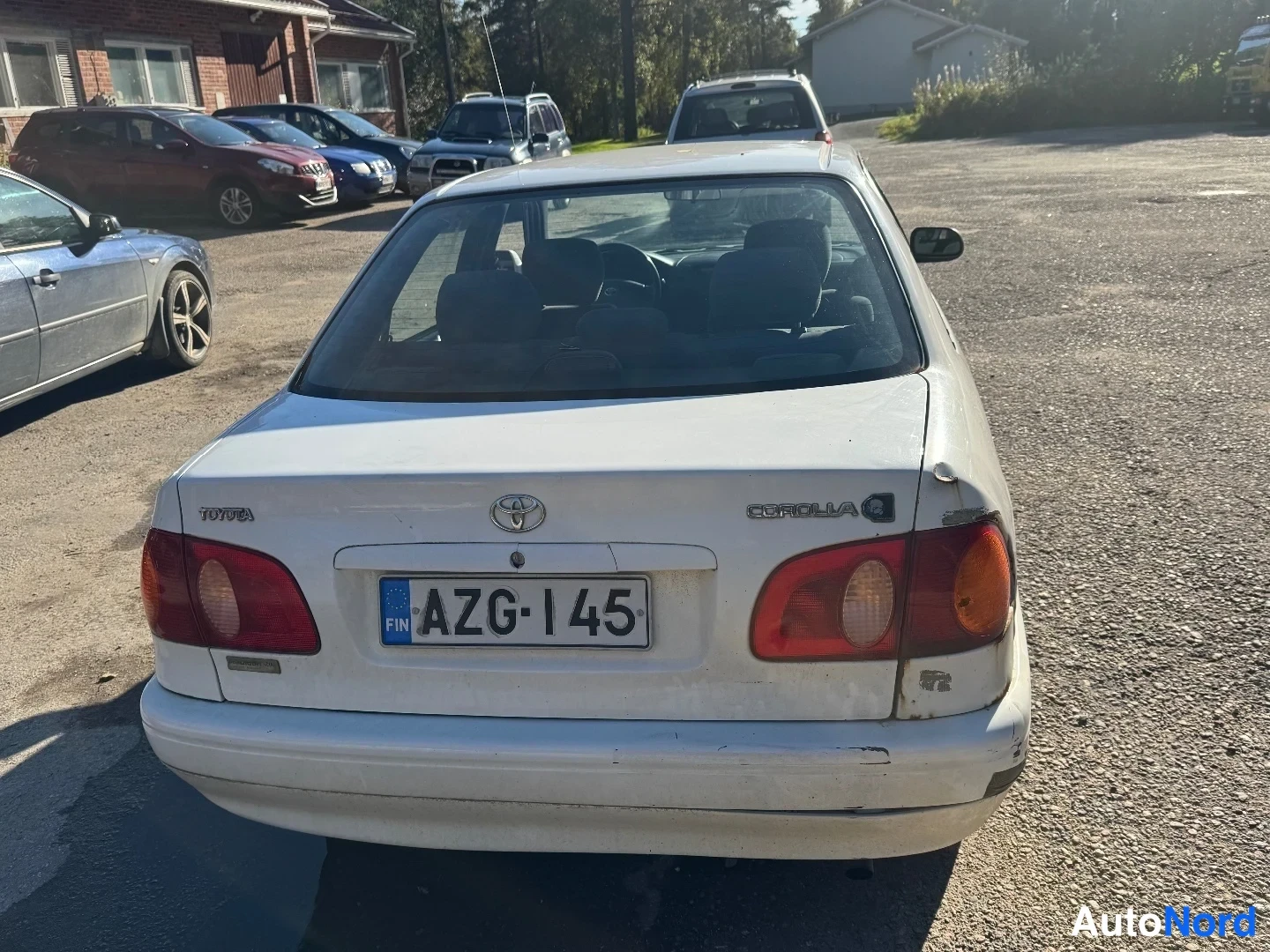 Takaa: Valkoisen Toyota Corolla -sedanin takapää; rekisterikilpi, takavalot ja bensan täyttöaukko auki.