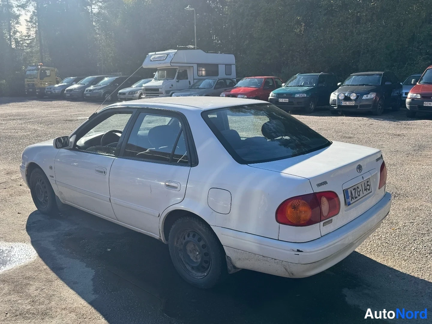 Takaviisto: Valkoinen Toyota Corolla -sedan takaviistosta: takavalo, moottoritila- ja tavaratilan kannet sekä vasen kylki näkyvissä, rekisterikilpi.