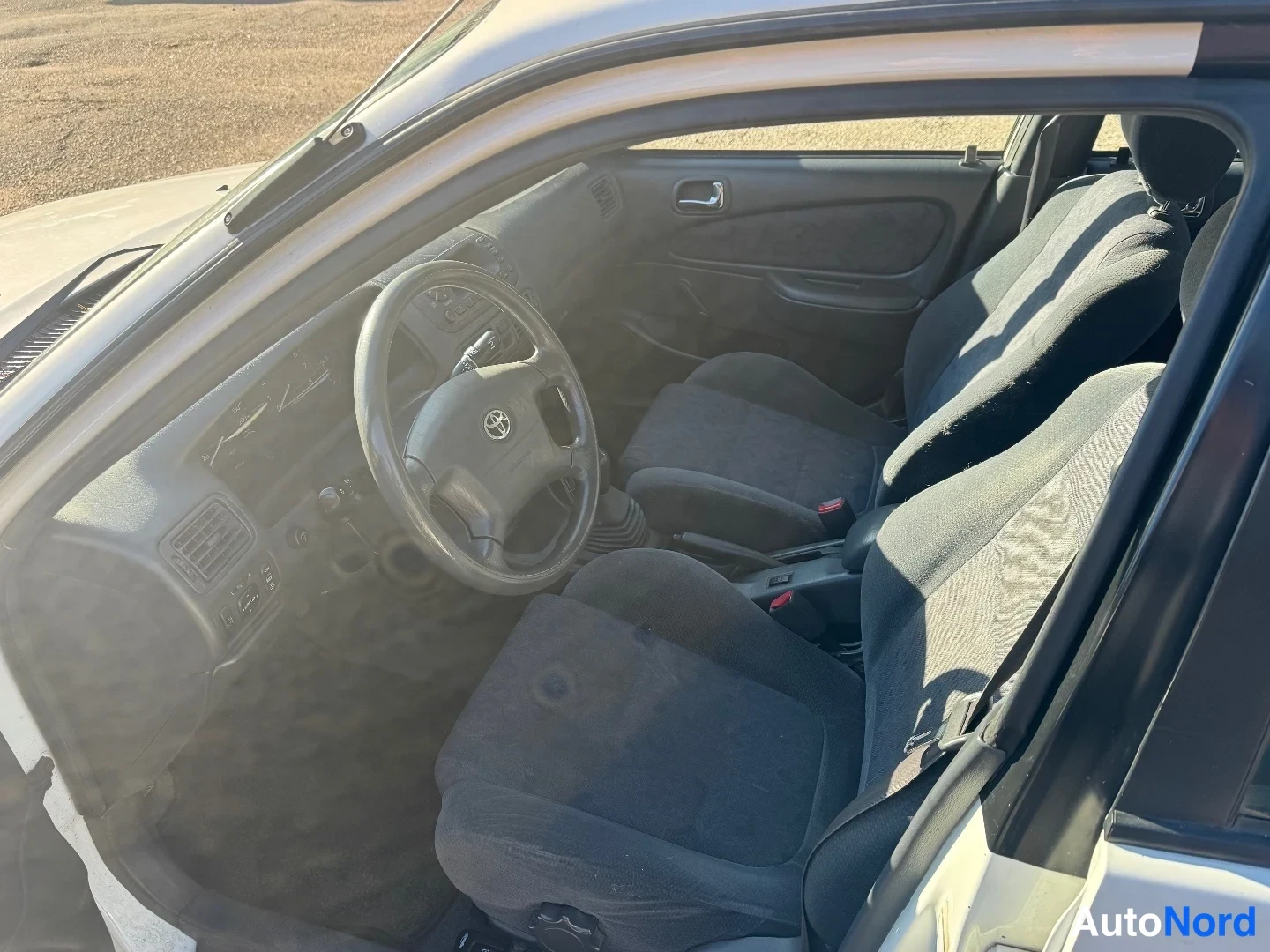 Muu: Auton sisätilat: Toyota-ohjauspyörä, tumma kojelauta ja kaksi tummaa kankaan etuistuinta, vaihtaja keskitunnelissa.