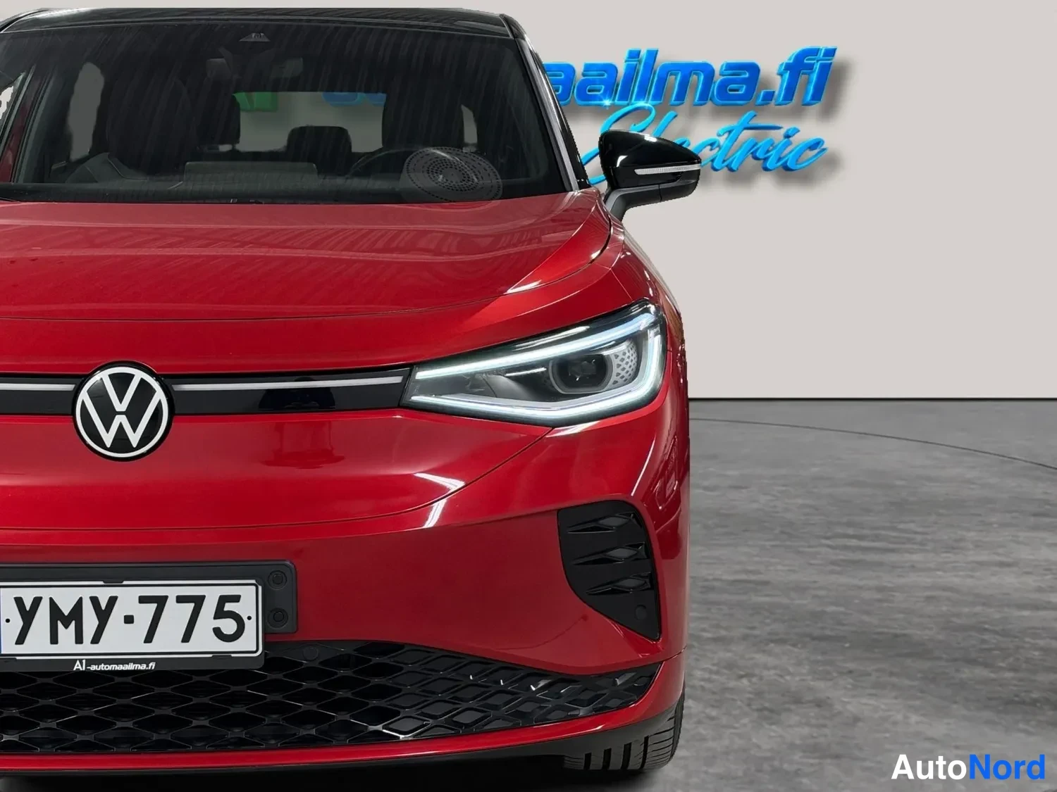Edestä: Punaisen Volkswagenin etupää lähikuvassa: pyöreä VW-tunnus, valaistu LED-etuvalo, musta alusäleikkö ja valkoinen rekisterikilpi.