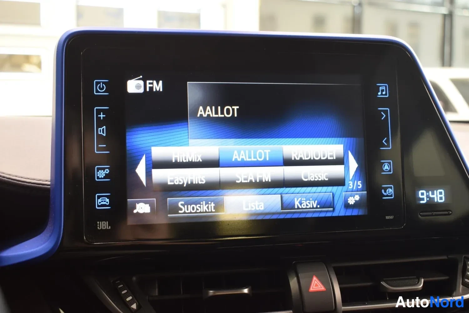 Yksityiskohta: Auton radioinfonäyttö: FM-viritys näyttää AALLOT-valikon kanavilla FitMix, SEA FM ja Classic; JBL-merkintä näytön alareunassa, kello näyttää 9:48.
