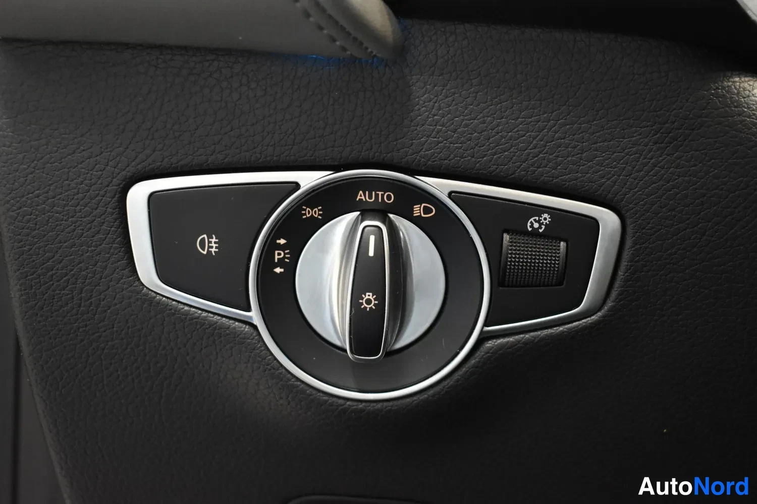 Yksityiskohta: Auton valokytkimen lähikuva: nupin ympärillä AUTO-merkintä sekä symbolit kaasuvaloille, seisontavaloille, lähivaloille ja sumuvaloille; vieressä pieni lisäkytki