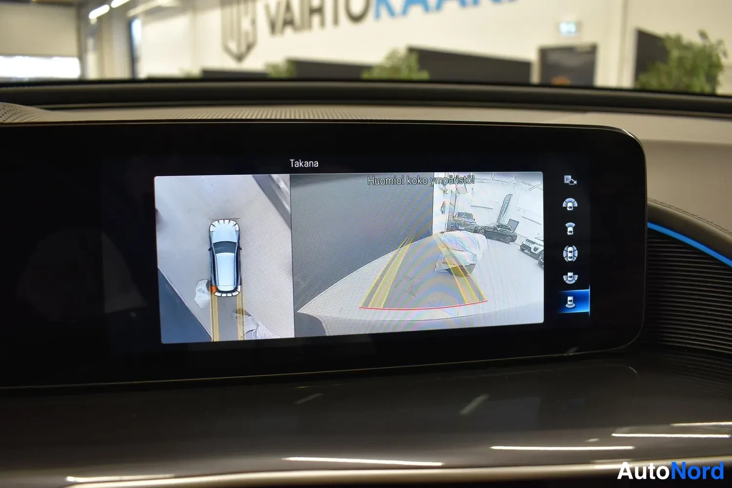 Edestä: Infotainment-näytössä peruutuskameran kuva ja ympäriview-näkymä ajoneuvon ollessa paikallaan; tekstit 'Takana' ja 'Huomioi koko ympäristö'.