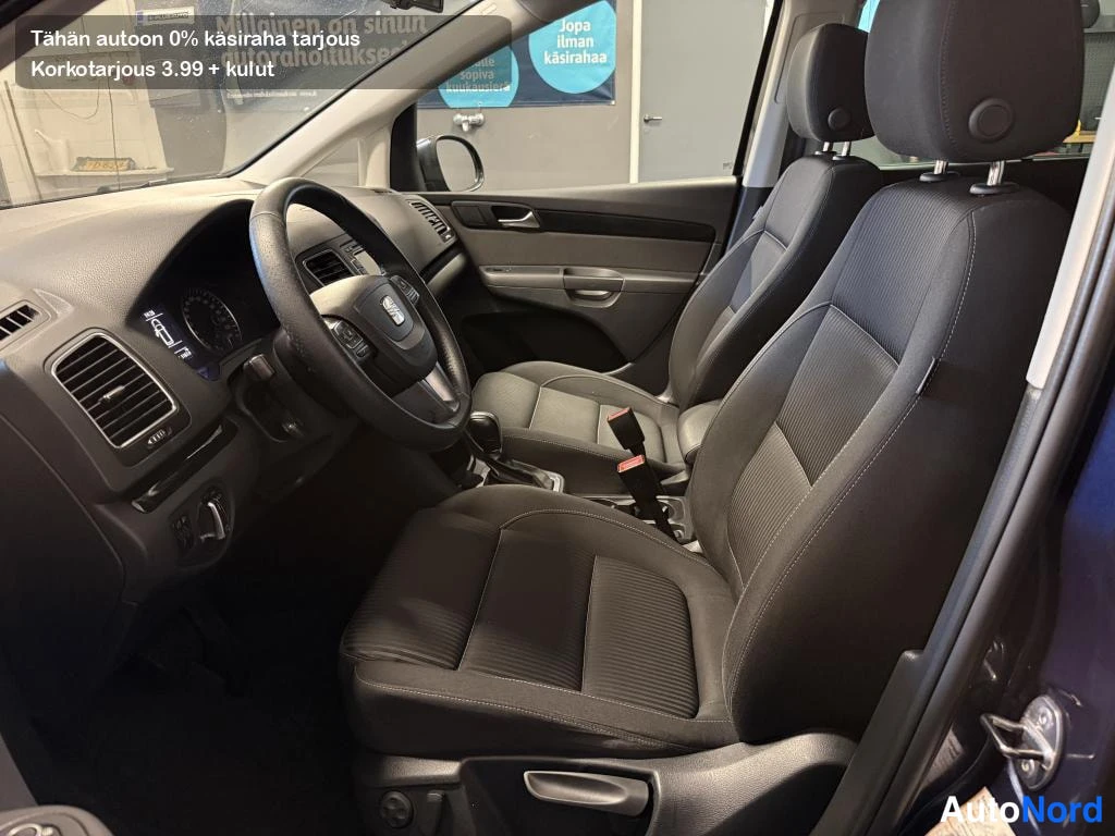 Edestä: Auton etuistuimet ja ohjaamo: mustat kankaanverhoillut istuimet, Seat-ohjauspyörä ja automaattivaihteen valitsin.