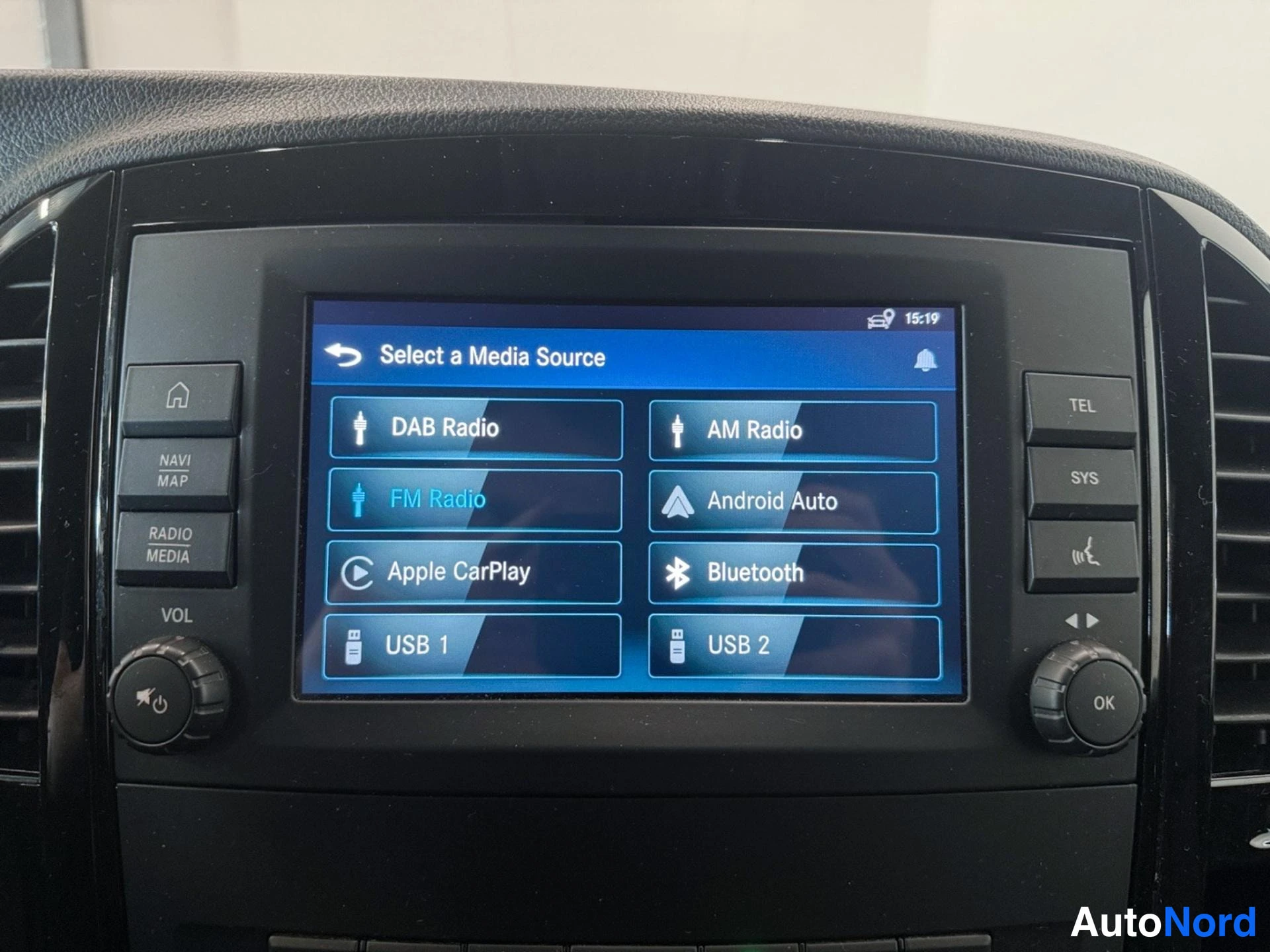 Yksityiskohta: Infotainment-näytön valikko 'Select a Media Source', jossa valittavana DAB Radio, AM Radio, FM Radio, Android Auto, Apple CarPlay, Bluetooth, USB 1 ja USB 2.