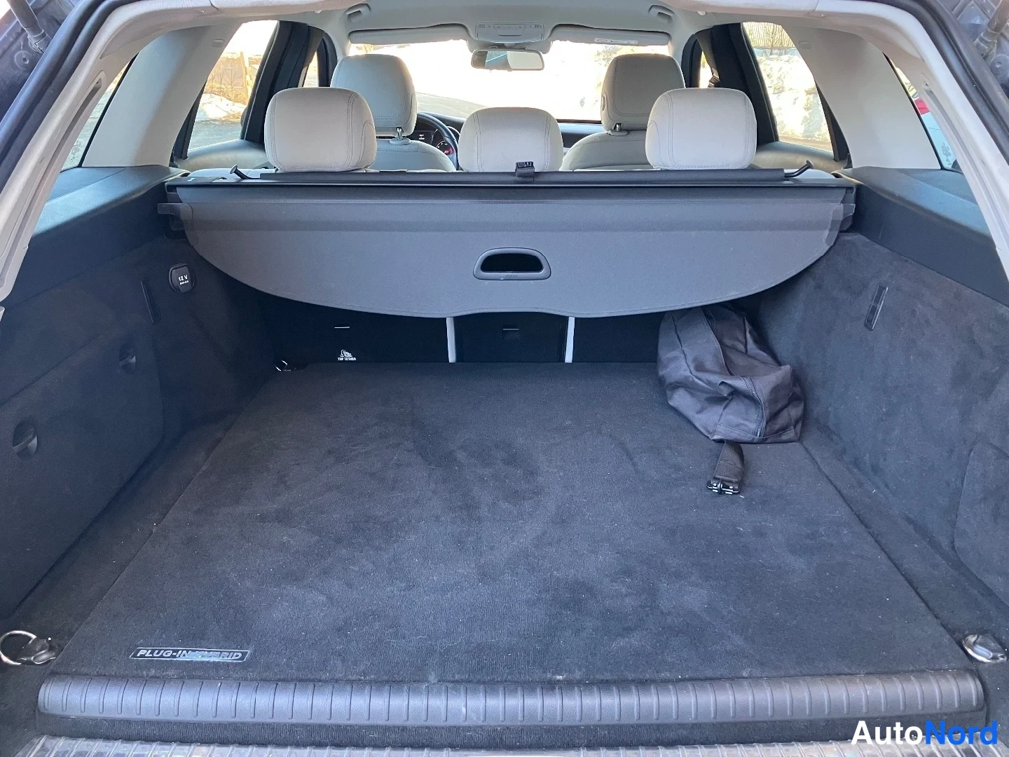 Tavaratila: Open trunk (cargo area) looking forward through the rear window toward the interior; luggage cover is raised; two dark headrests visible in front of it; floor m