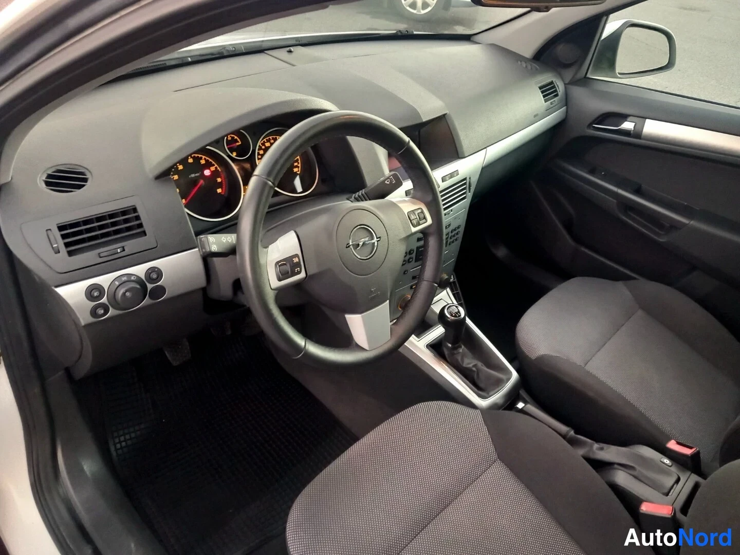 Etuviisto, nokka oikealle: Volkswagen Golin ohjaamo vasemmalta etualalta kuvattuna: Opel-logollinen ohjauspyörä, analogiset mittarit, manuaalivaihteisto ja tummat kangasistuimet.