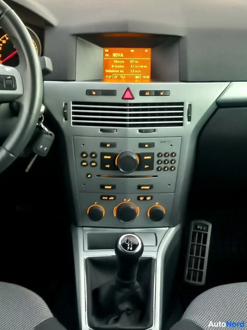 Yksityiskohta: Kojelaudan ja keskikonsolin näkymä: käytävaihteen vaihdekeppi, radiopaneeli ja oranssi näyttö, jossa lukee mm. NOVA ja Radiovyöhyke 237 km.