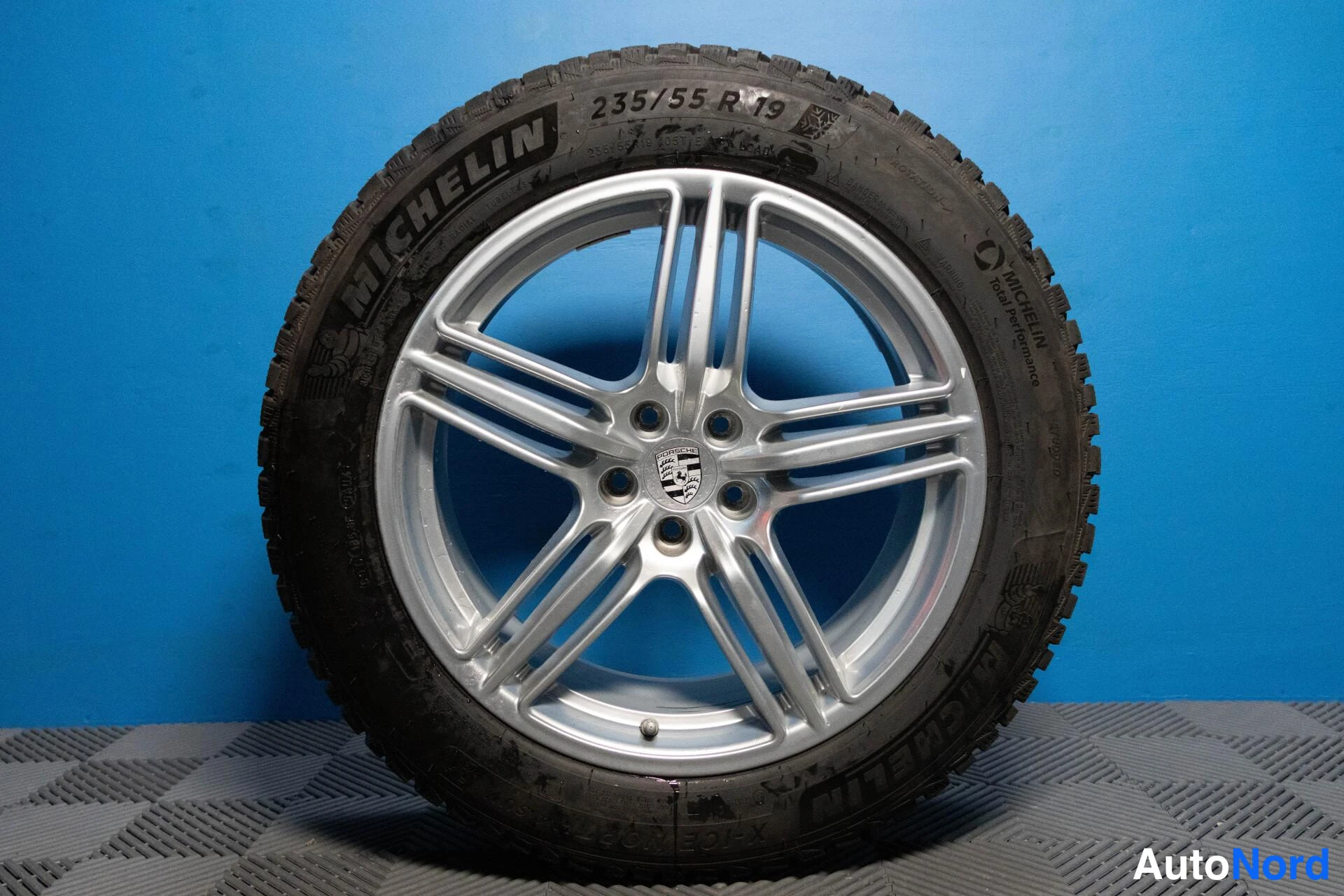 Yksityiskohta: Hopeavanteella varustettu Michelin-kitkarengas, kokomerkintä 235/55 R 19, sinistä taustaa vasten.