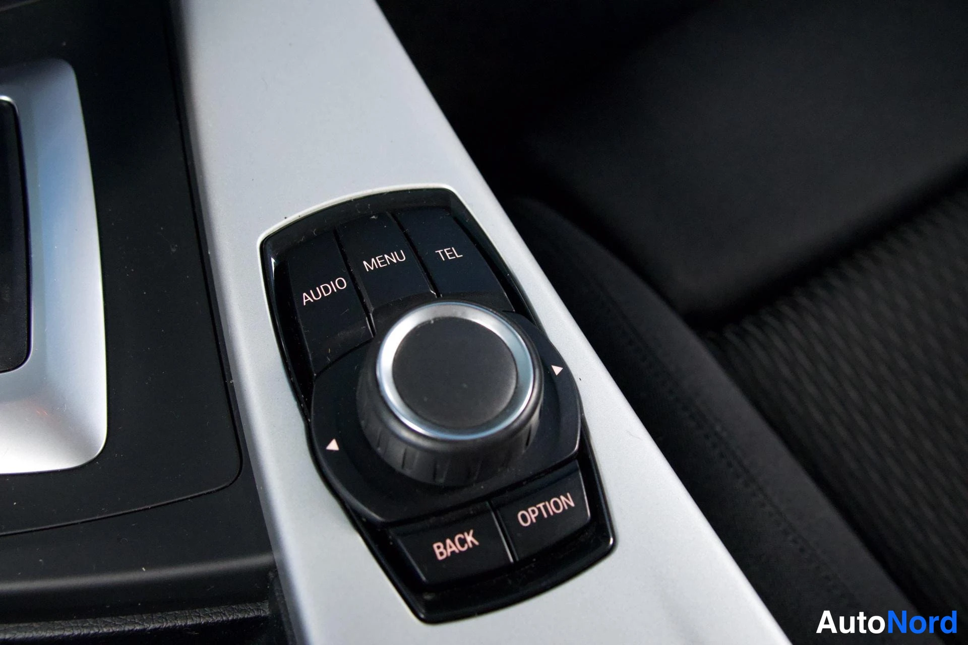Yksityiskohta: Auton sisätilan keskikonsolin iDrive-ohjain, jossa pyörre ohjain ja näppäimet AUDIO, MENU, TEL, BACK ja OPTION.