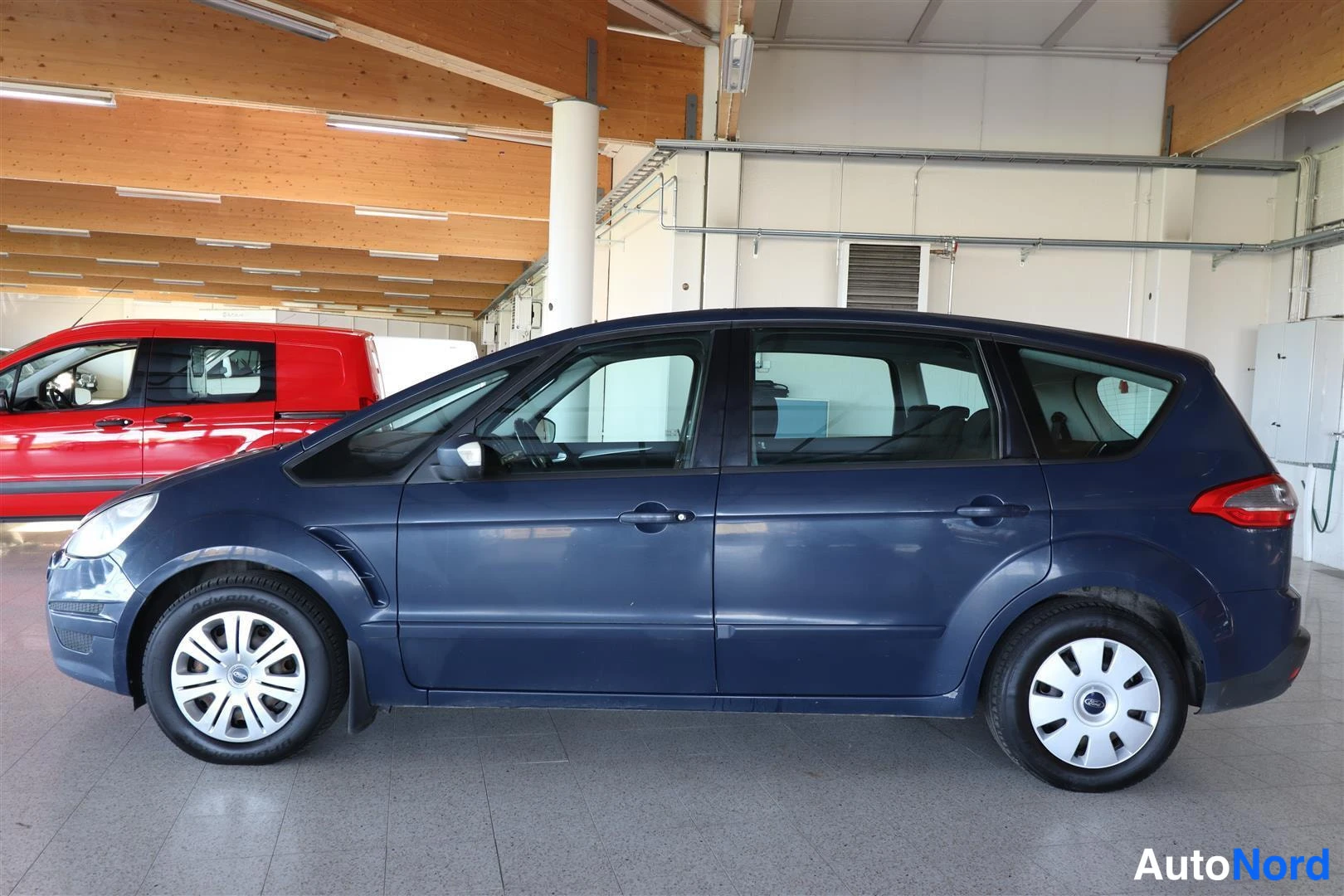 Sivulta: Tummansininen Ford S-MAX sivulta kuvattuna autonvaihtohallissa.
