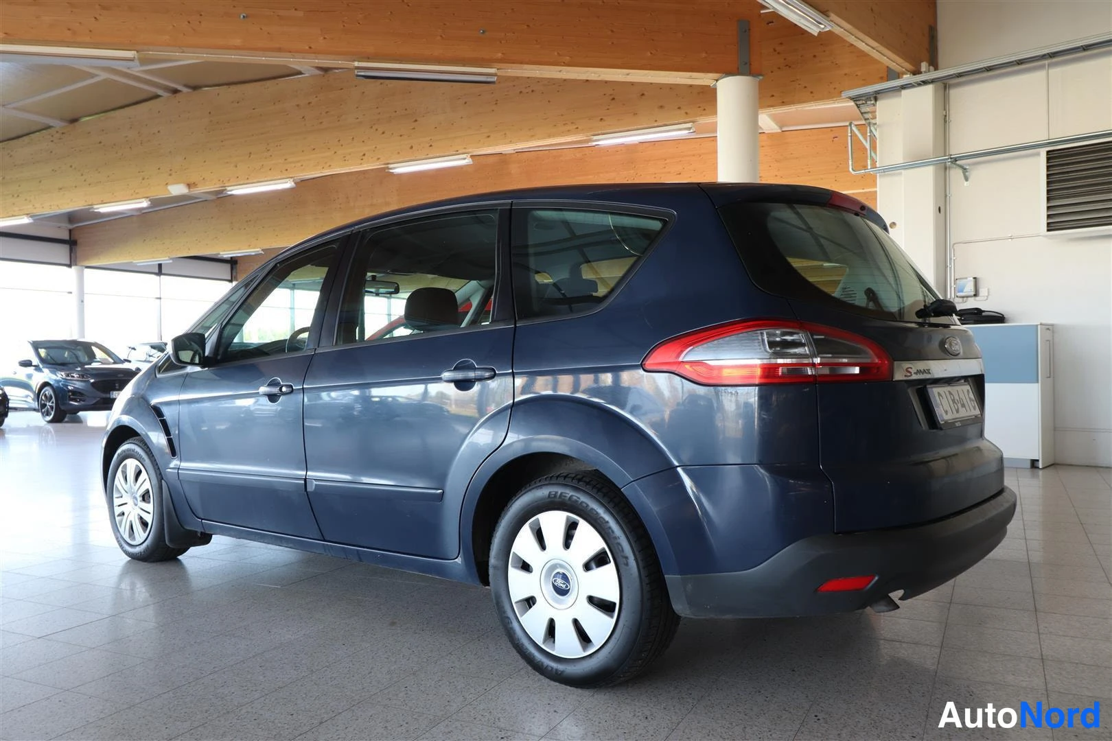 Takaviisto: Tummansininen Ford S-MAX takaosaviistossa oikealta kuvattuna hallissa, takavalot ja rekisterikilpi näkyvät.