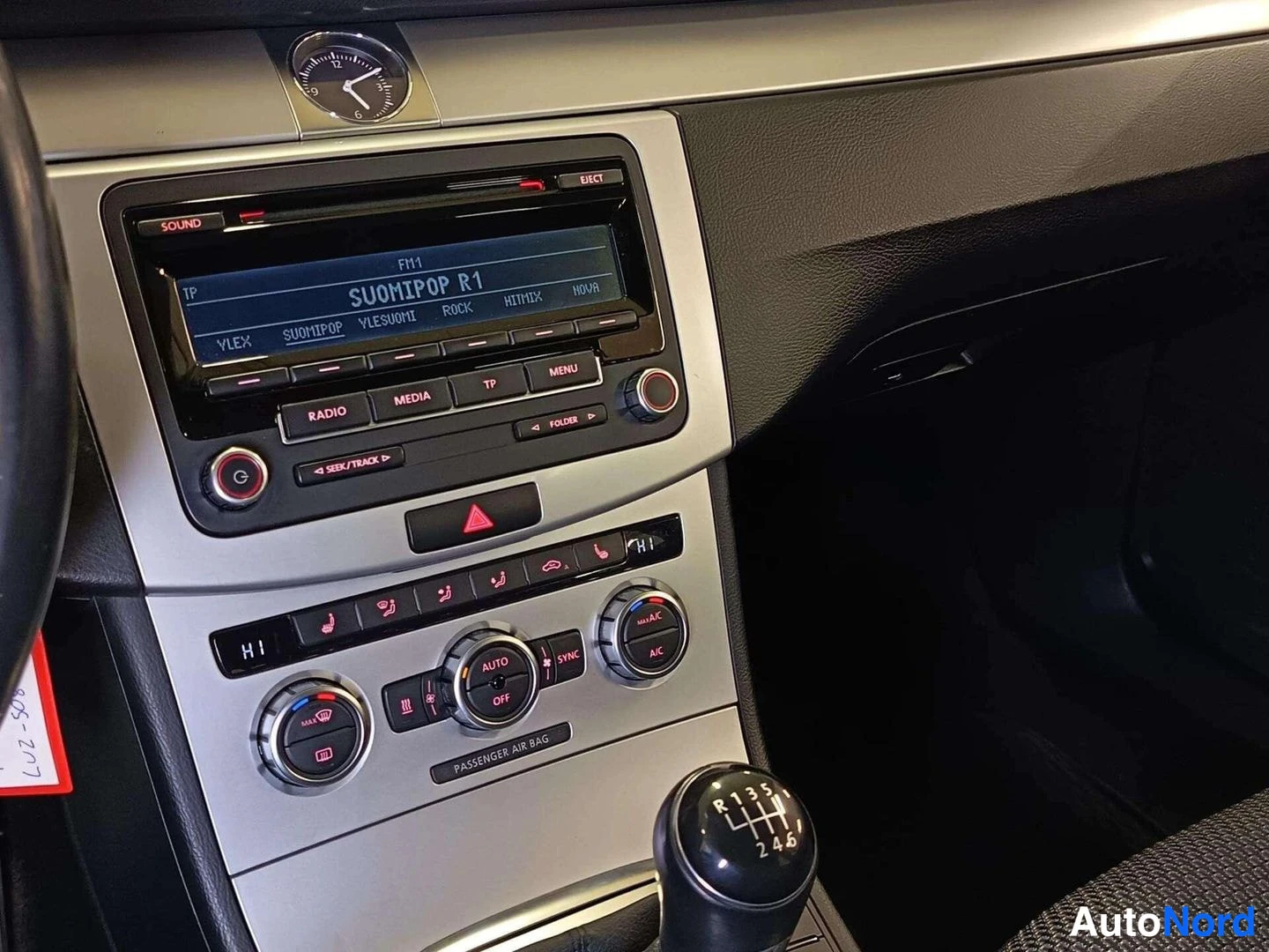 Edestä: Kojelaudan keskiosa: radiopaneeli näytöllä SUOMIPOP R1, ilmastointiautomaation AUTO-, SYNC- ja A/C-napit, varoitusvilkkunappi ja 6-vaihteinen manuaalivaihteen k