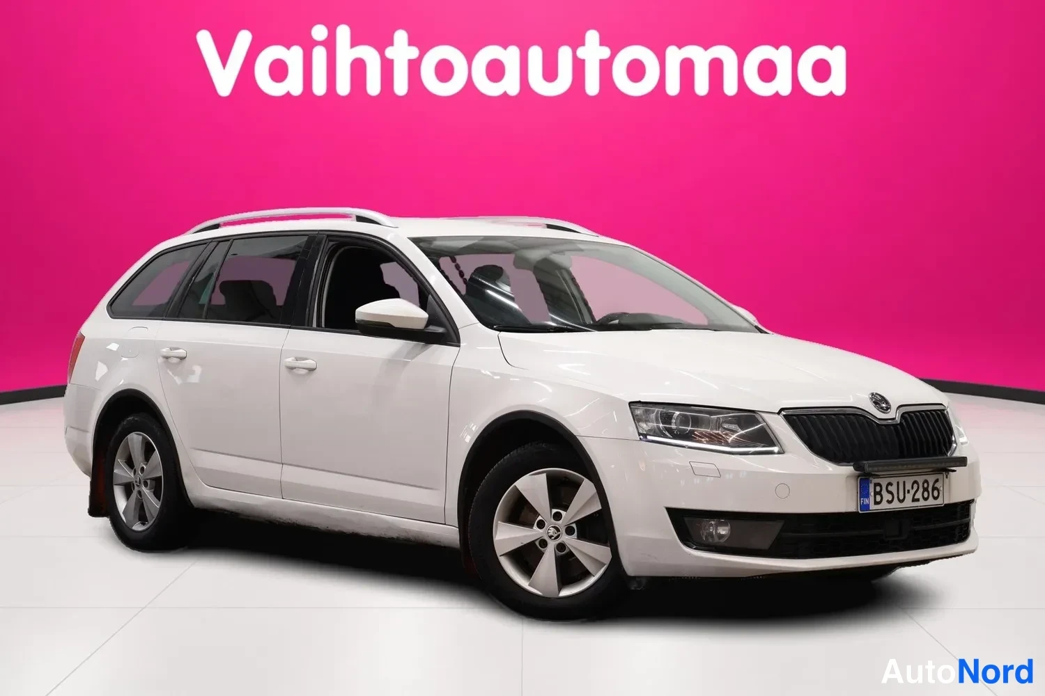 Etuviisto, nokka oikealle: Valkoinen farmariauto kuvattu etulokasuunnasta, rekisterikilpi, katolla kattotankokiskot.