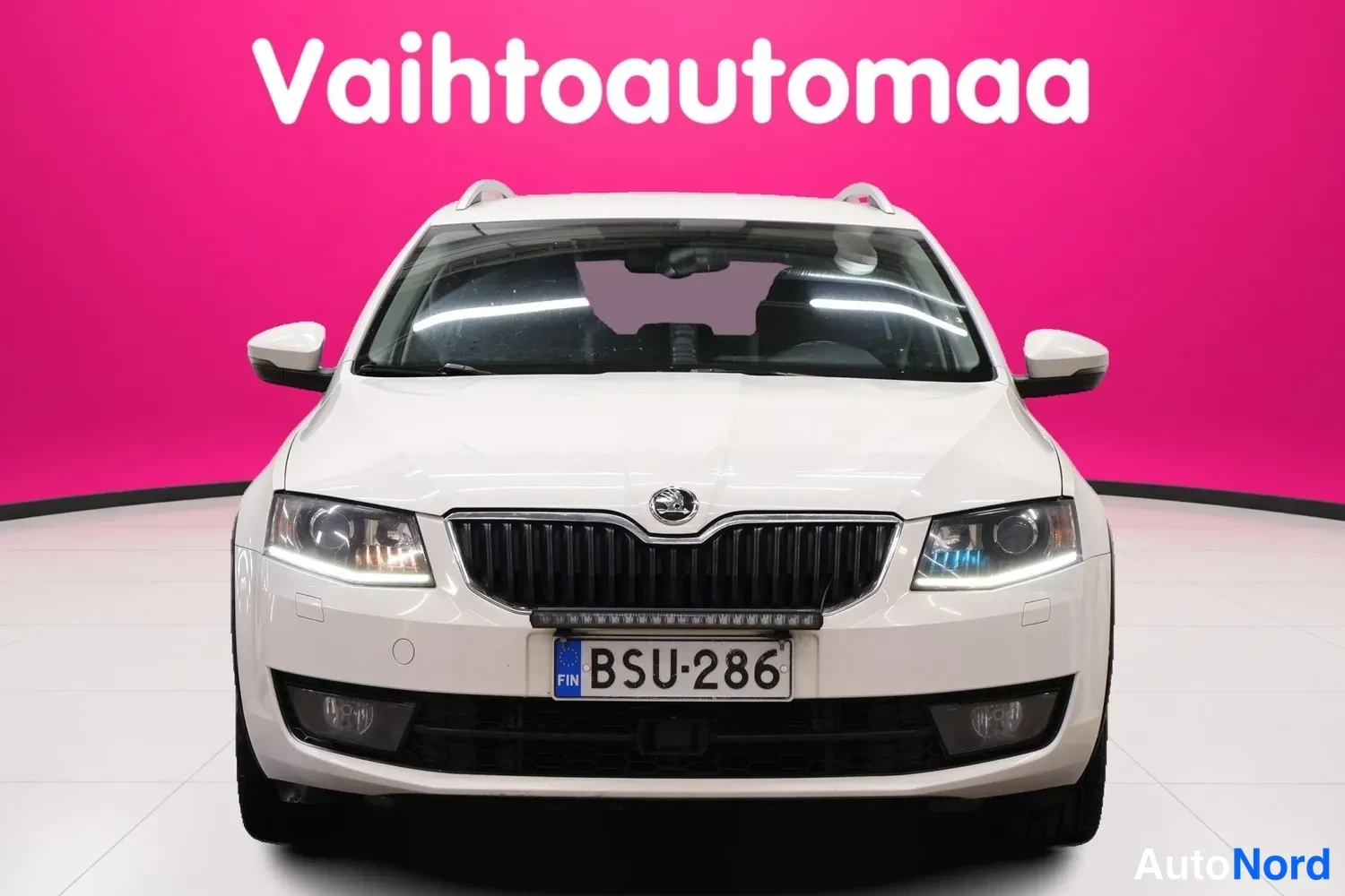 Edestä: Valkoisen farmariauton suora etunäkymä, škoda-merkki säleikkössä, rekisterikilpi.